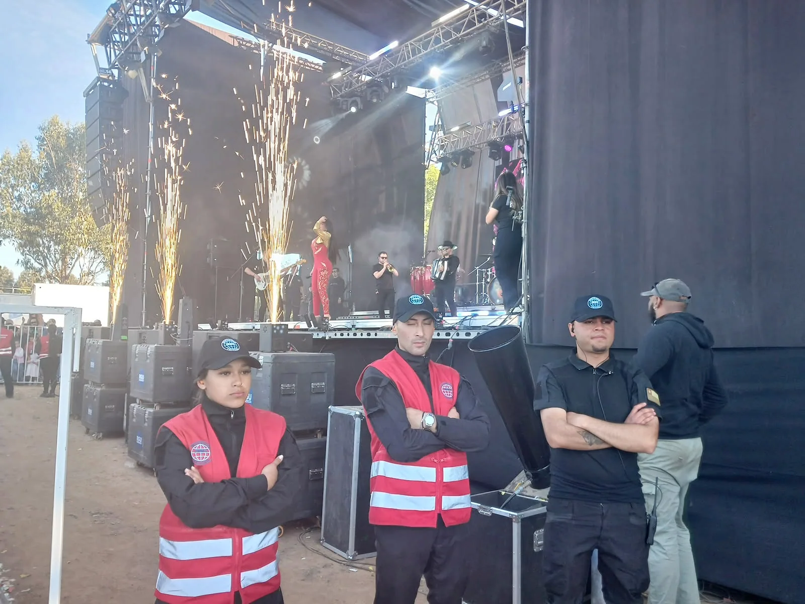 Guardias con chalecos rojos y negros frente a escenario con efectos de luz
