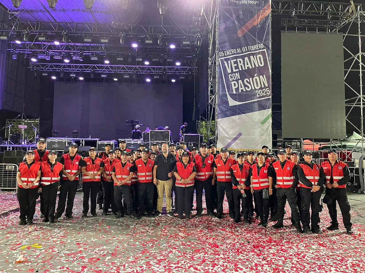 Grupo numeroso de guardias en chalecos rojos ante un escenario con lona de evento